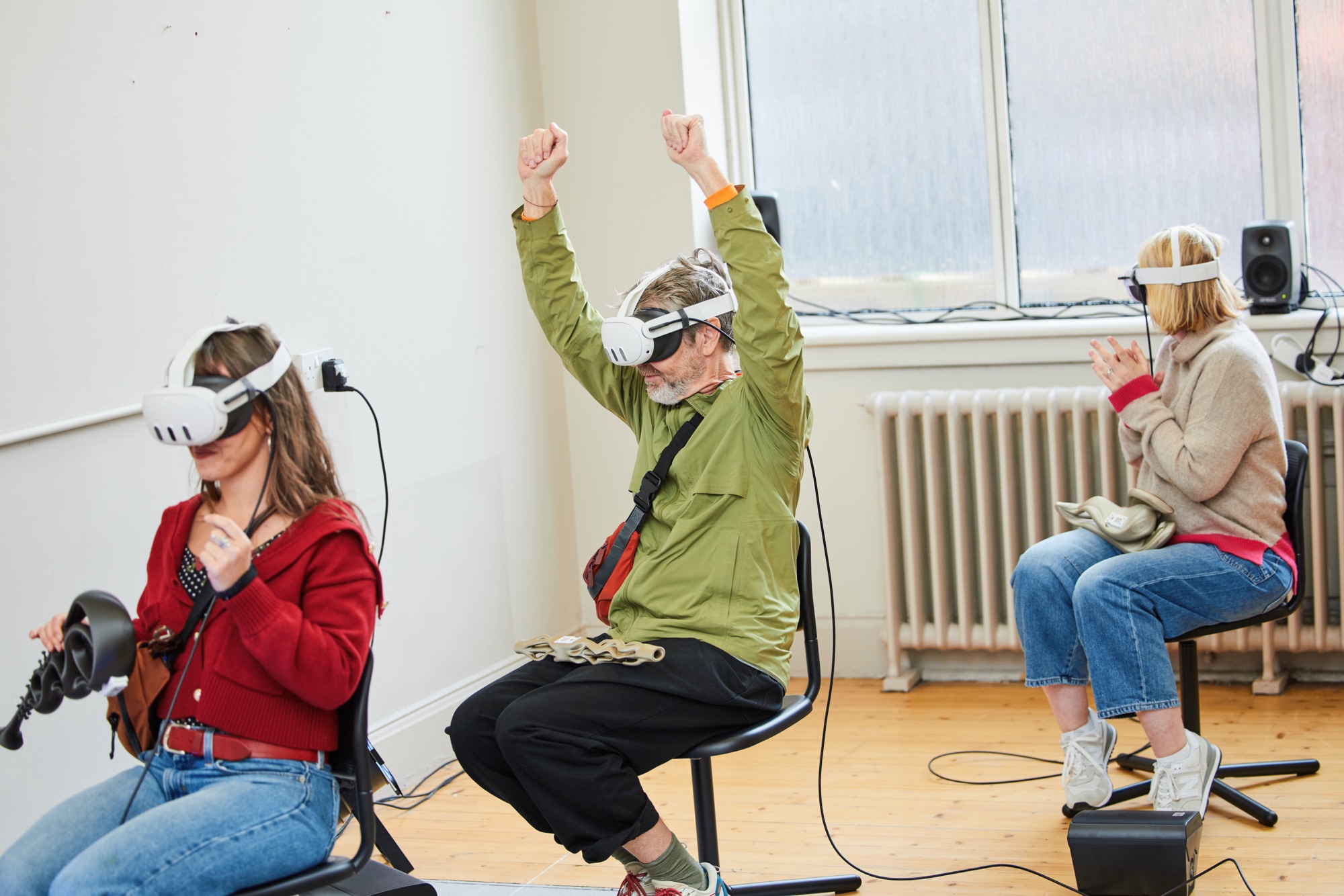 Three participants seated in headsets, arms raised mid-performance
